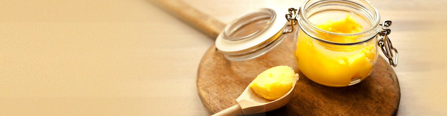 A jar of golden, grass-fed ghee with a wooden spoon on a rustic wooden board, highlighting its rich texture and purity.